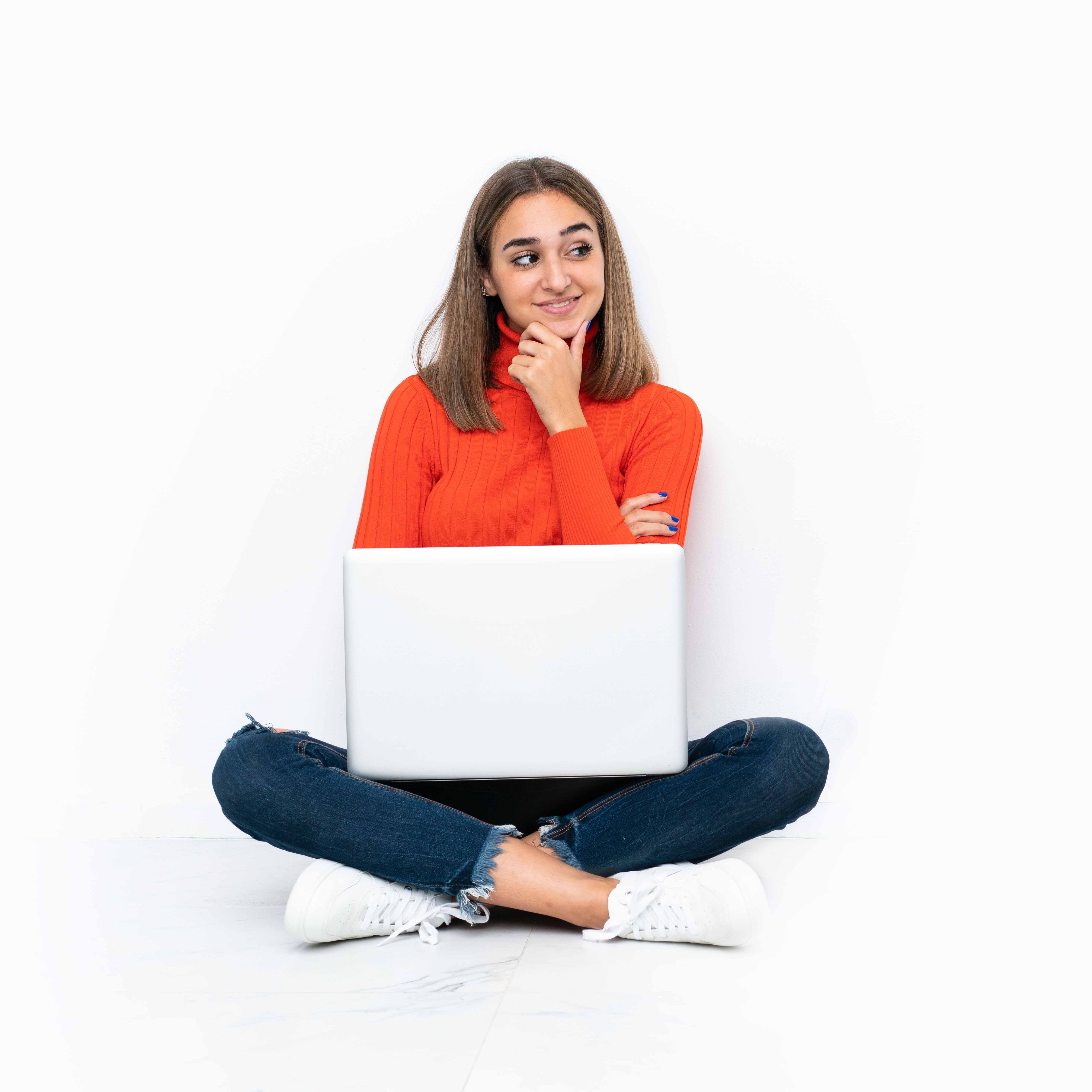 Young caucasian woman sitting on the floor with a laptop looking to the side